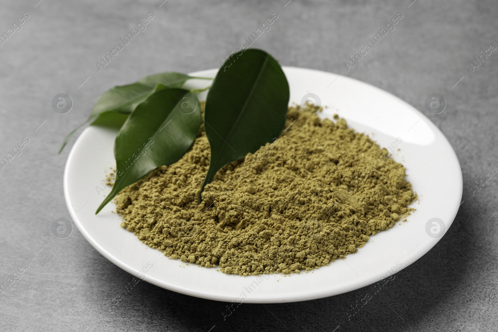 Photo of Henna powder and green leaves on grey background. Natural hair coloring