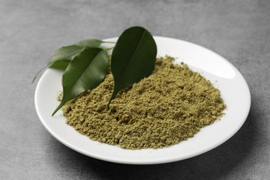 Henna powder and green leaves on grey background. Natural hair coloring