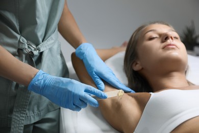 Young woman undergoing hair removal procedure of armpits with sugaring paste in salon