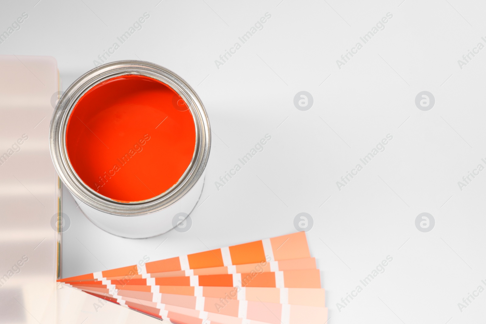 Photo of Can of orange paint and color samples on white background, above view