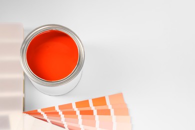Photo of Can of orange paint and color samples on white background, above view