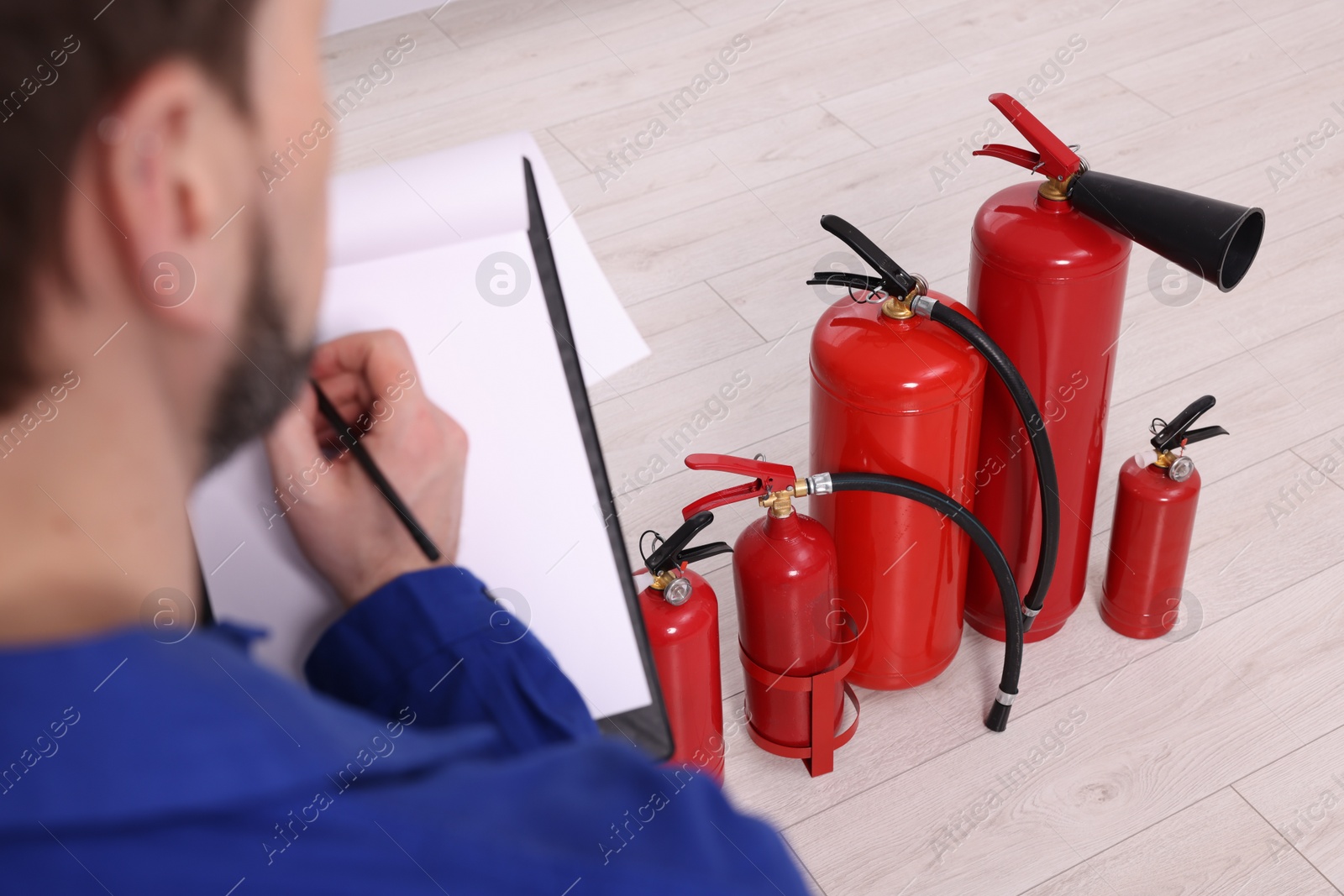 Photo of Man with clipboard checking fire extinguishers indoors, closeup