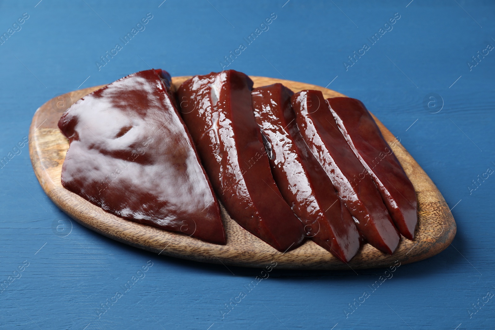 Photo of Cut raw beef liver on blue wooden table, closeup