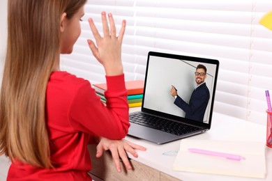 Image of E-learning. Little girl raising her hand to answer during online lesson at table indoors