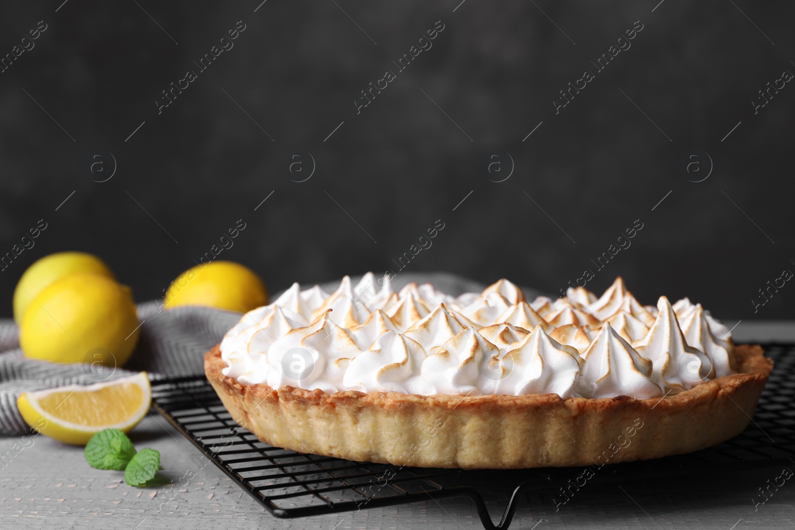 Photo of Cooling rack with delicious lemon meringue pie on grey table