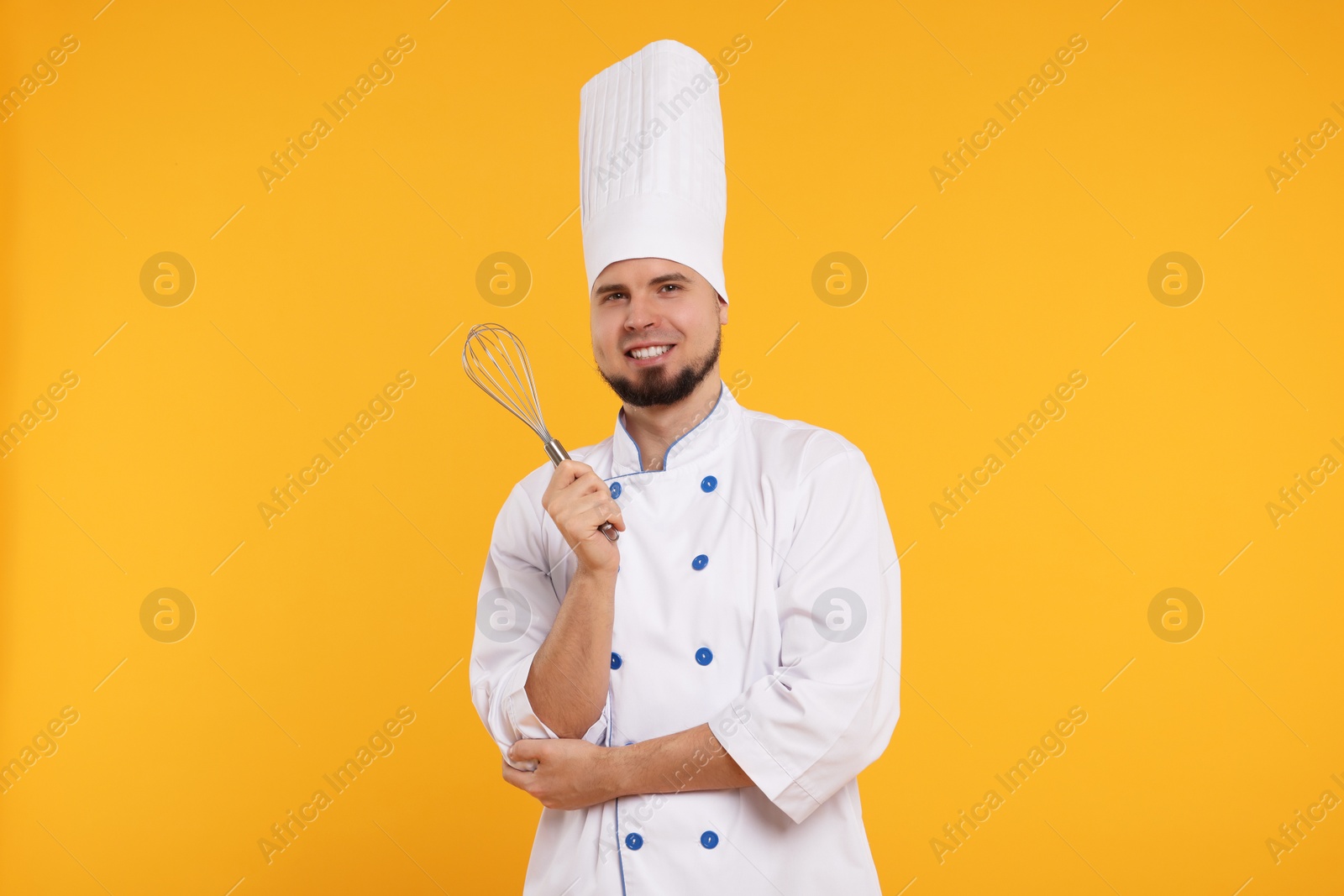 Photo of Happy professional confectioner in uniform holding whisk on yellow background