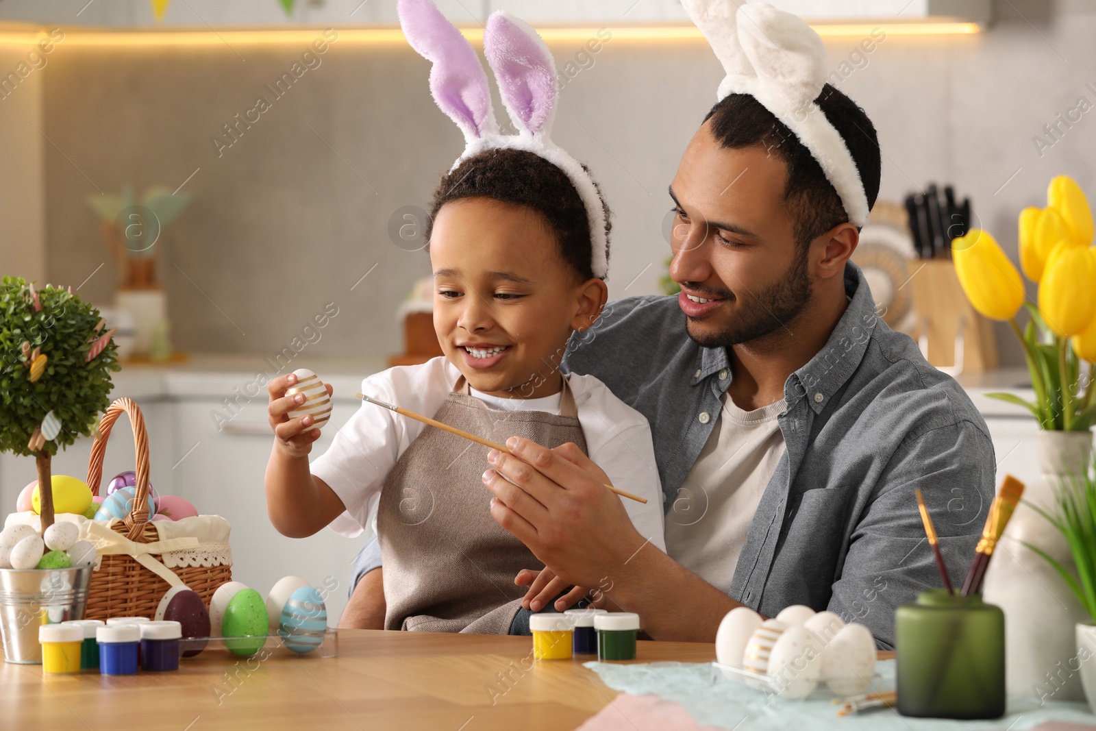 Photo of Happy African American father and his cute son painting Easter eggs at table in kitchen