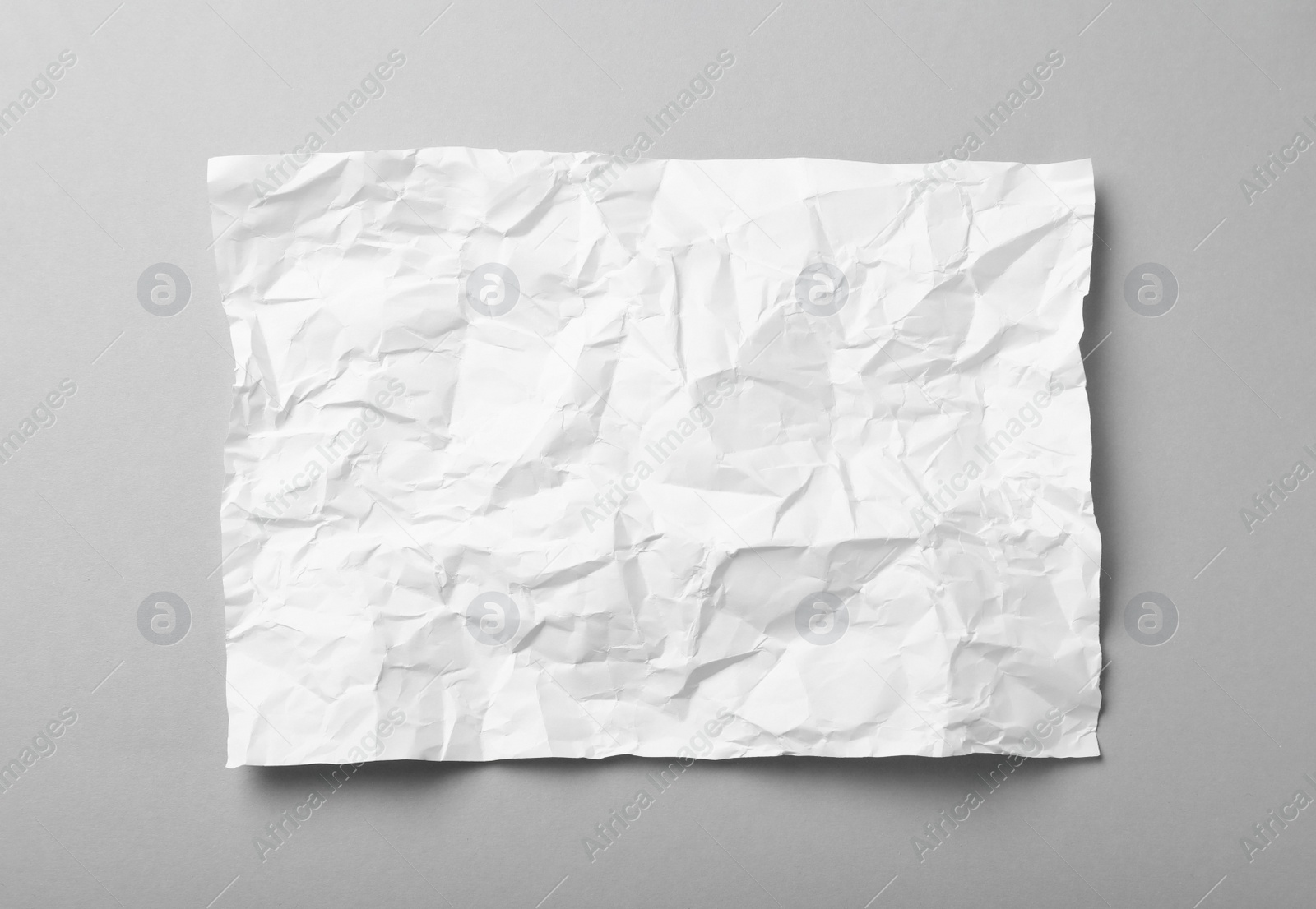 Photo of Sheet of white crumpled paper on grey background, top view