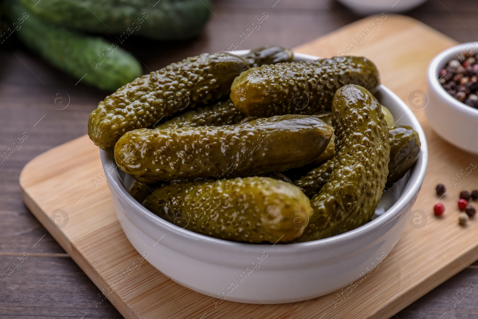 Photo of Bowl of pickled cucumbers and ingredients for food preservation on wooden table, closeup