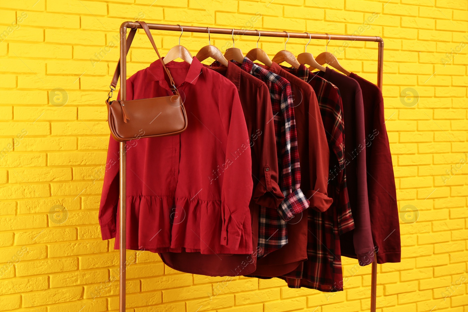 Photo of Rack with stylish clothes and bag near yellow brick wall