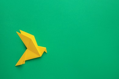 Photo of Beautiful yellow origami bird on green background, top view. Space for text