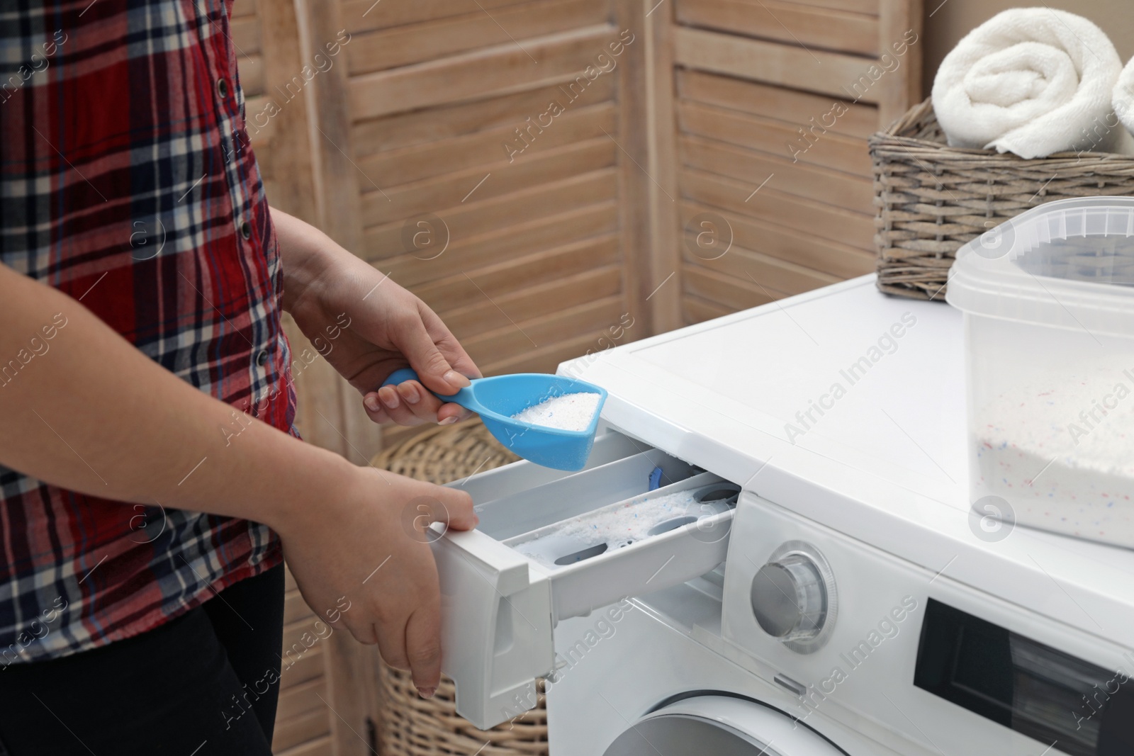 Photo of Woman pouring detergent powder into washing machine in laundry room, closeup