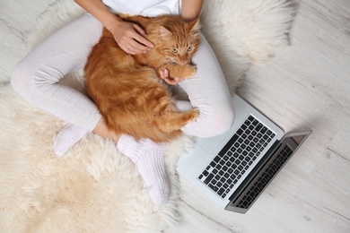 Photo of Woman with cute red cat and laptop on fur carpet, top view