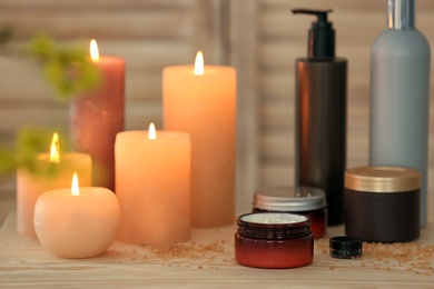 Photo of Body care cosmetics and burning candles on table