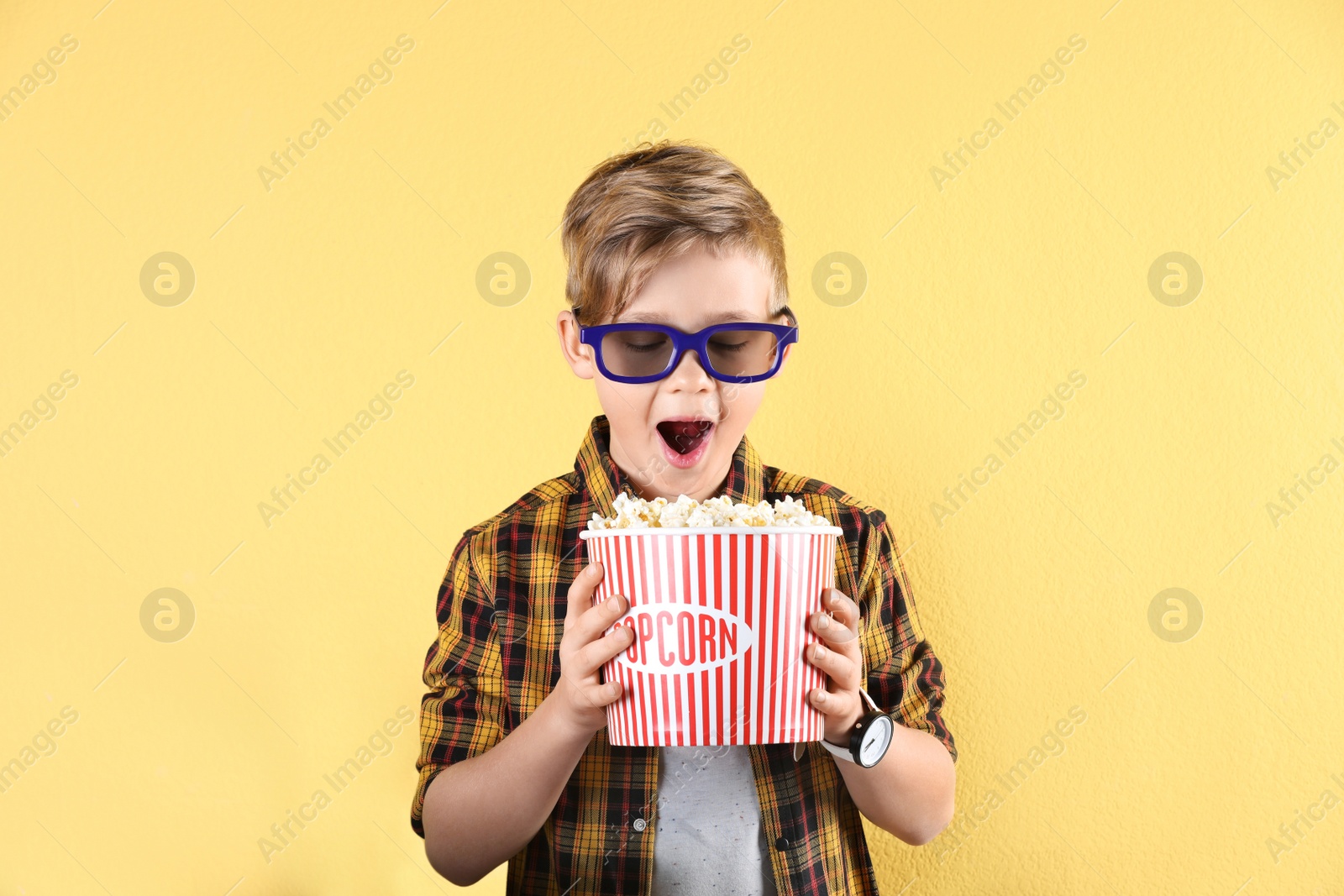 Photo of Cute boy in 3D glasses with popcorn bucket on color background