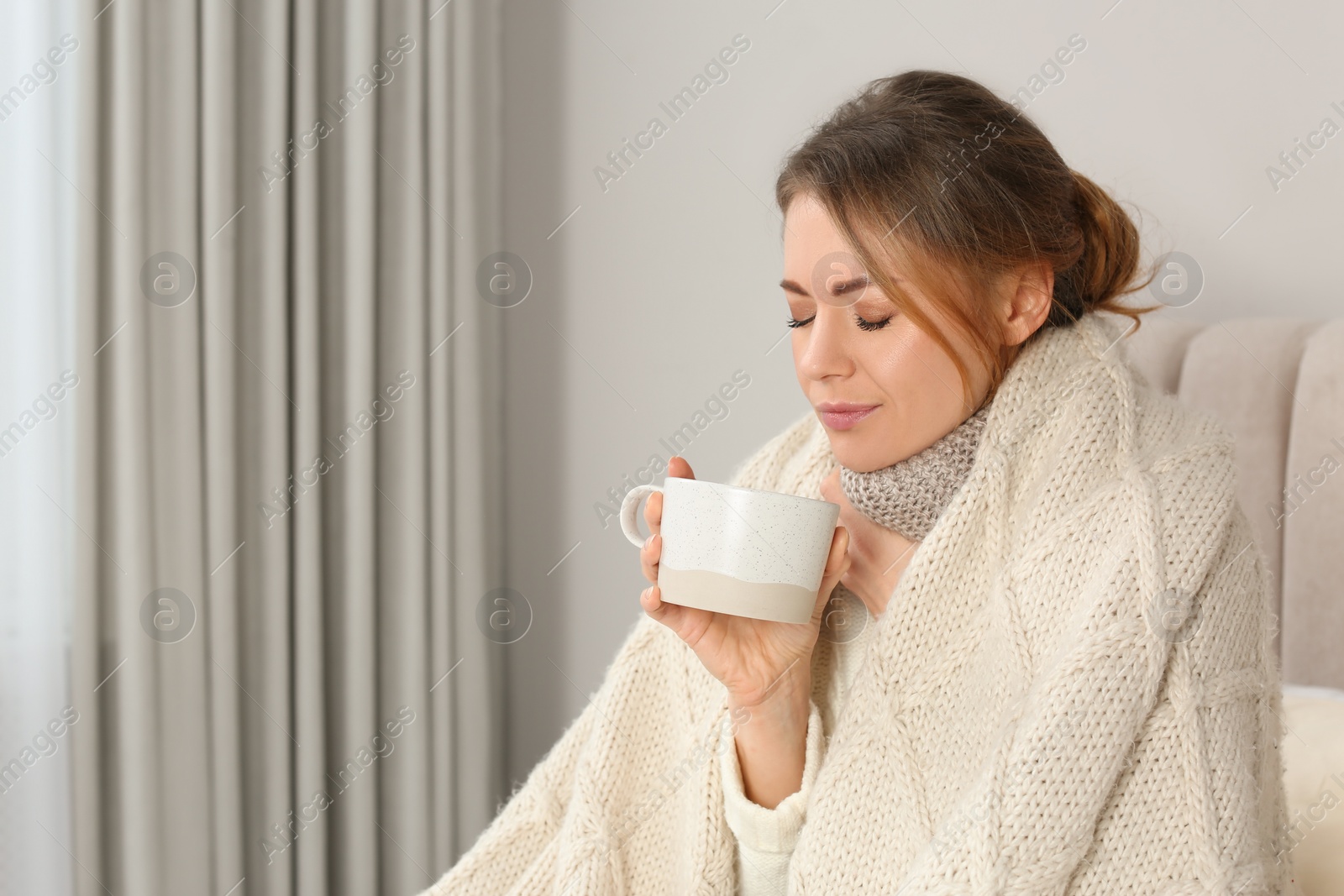Photo of Sick woman with warm plaid and cup of drink in bed at home