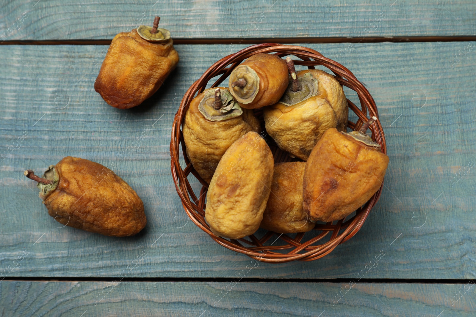 Photo of Wicker basket with tasty dried persimmon fruits on light blue wooden table, flat lay