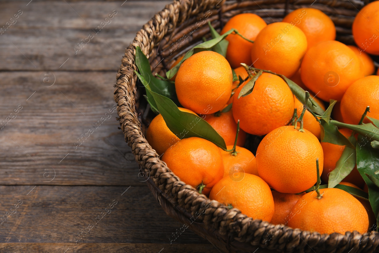 Photo of Fresh ripe tangerines in wicker basket on wooden table. Space for text