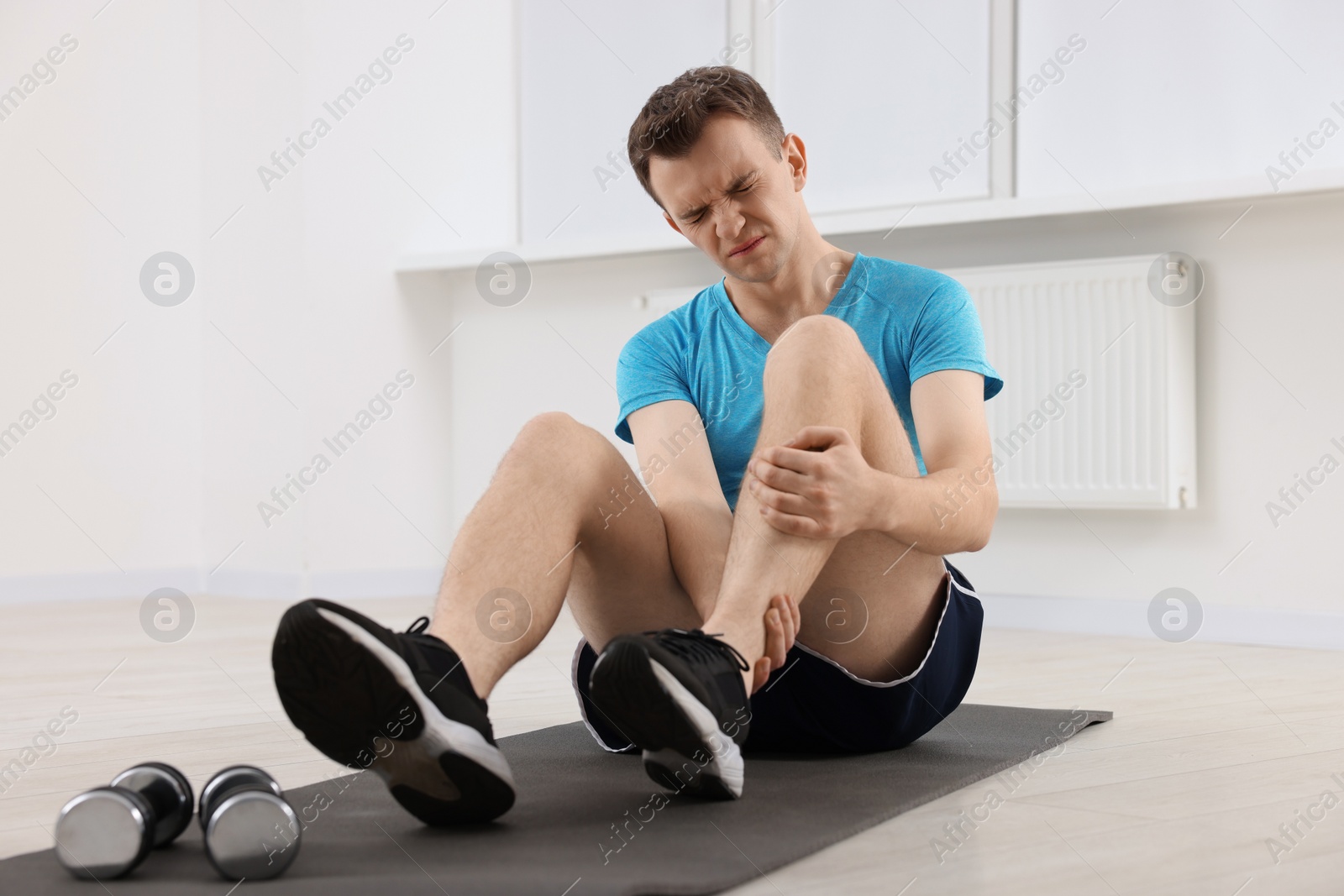 Photo of Man suffering from leg pain on mat indoors