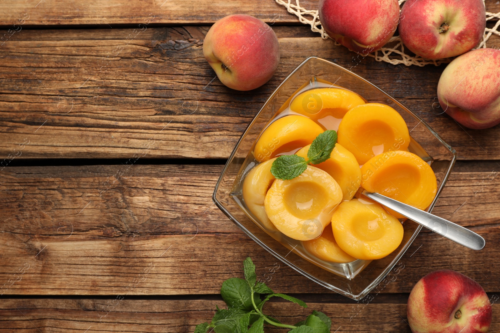 Photo of Canned peach halves in glass bowl on wooden table, flat lay. Space for text