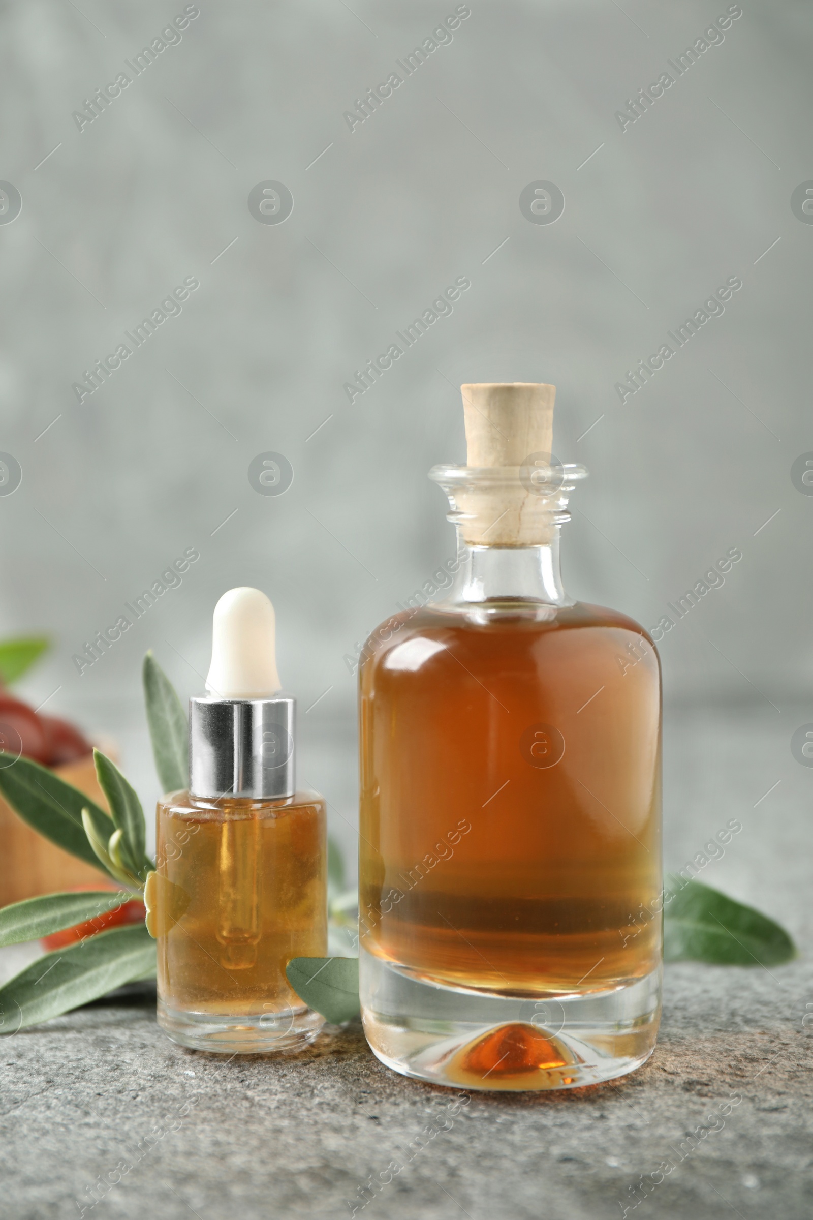 Photo of Glass bottles with jojoba oil on stone table against grey background