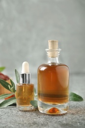 Photo of Glass bottles with jojoba oil on stone table against grey background