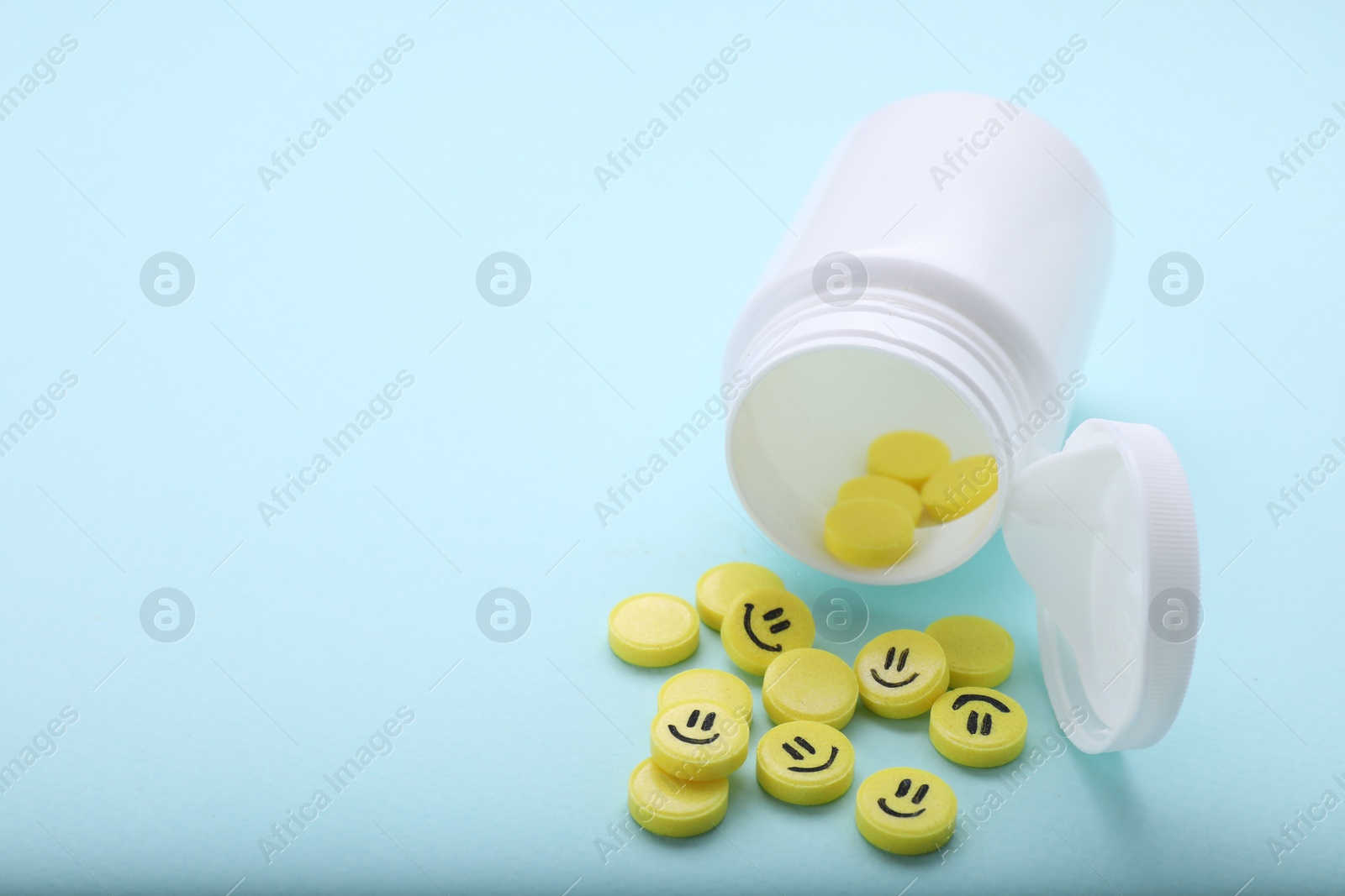 Photo of Yellow antidepressants with happy emoticons and medical bottle on light blue background, closeup. Space for text