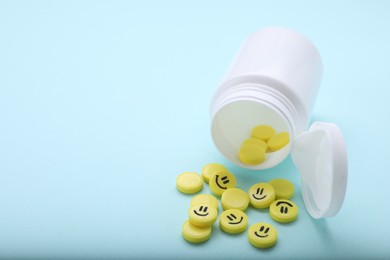 Yellow antidepressants with happy emoticons and medical bottle on light blue background, closeup. Space for text