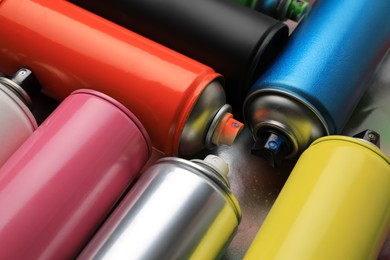 Cans of different graffiti spray paints on color background, closeup