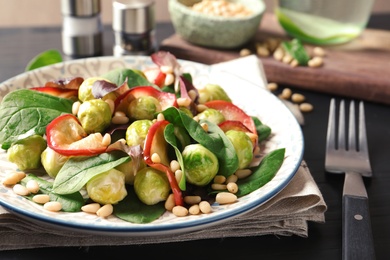 Photo of Plate of delicious salad with Brussels sprouts and roasted apples on wooden table