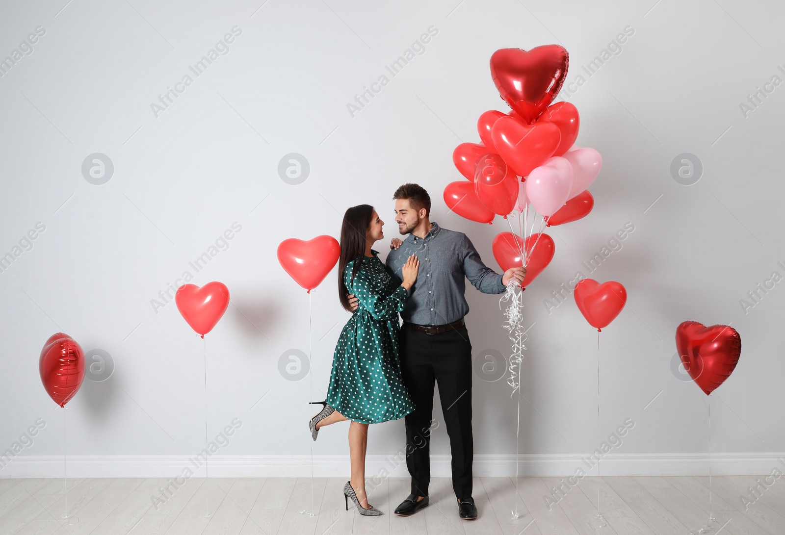 Photo of Happy young couple with heart shaped balloons near light wall. Valentine's day celebration