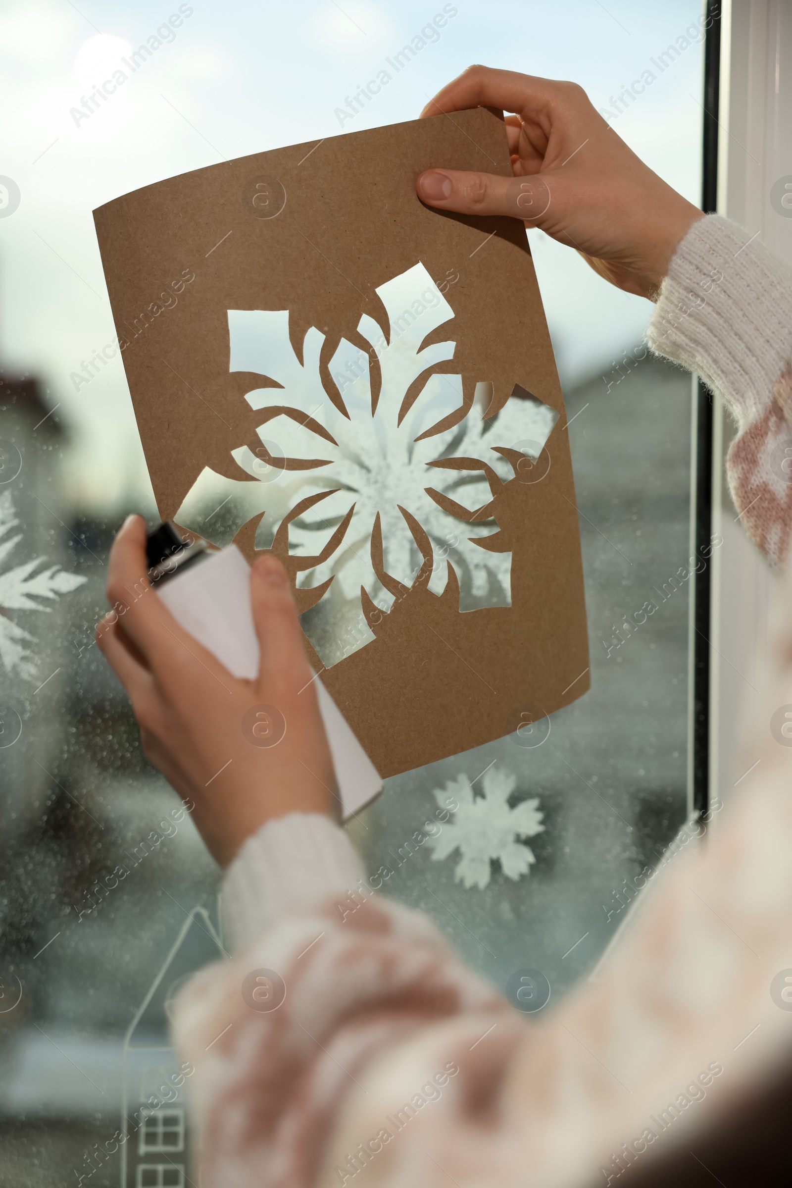 Photo of Woman using snow spray for decorating window with snowflakes at home, closeup