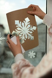 Woman using snow spray for decorating window with snowflakes at home, closeup