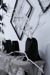 Black frames with web on white wall and branches in vase on fireplace decorated for Halloween indoors