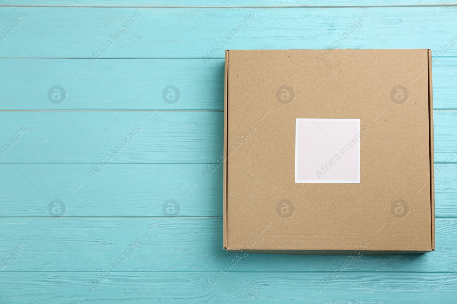 Photo of Cardboard box on light blue wooden background, top view. Space for text