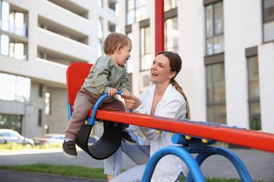 Happy nanny and cute little boy on seesaw outdoors