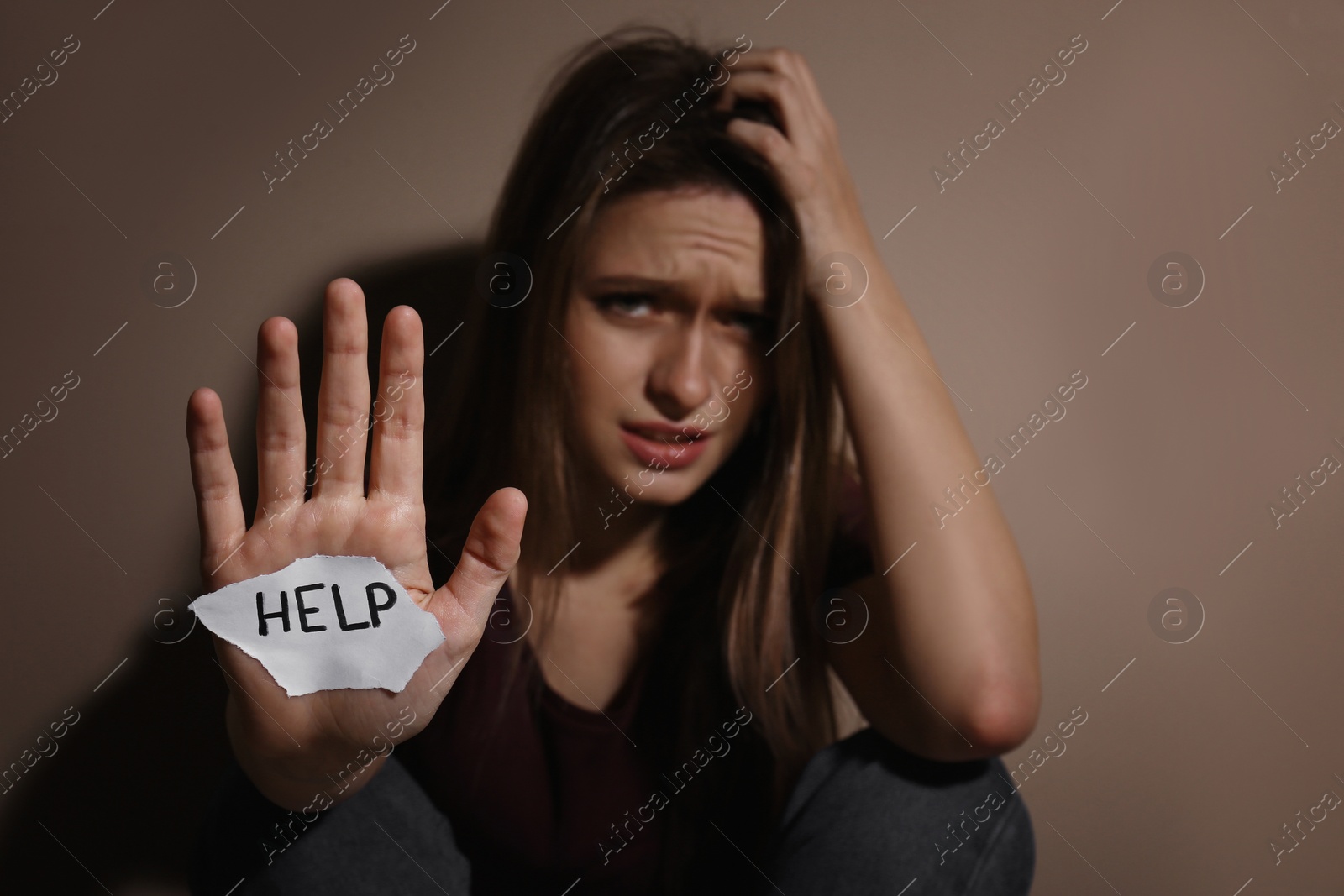 Photo of Abused young woman with sign HELP near beige wall, focus on hand. Domestic violence concept