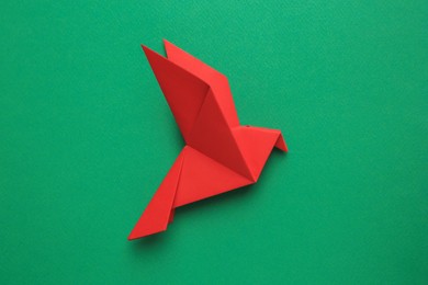 Photo of Beautiful red origami bird on green background, top view