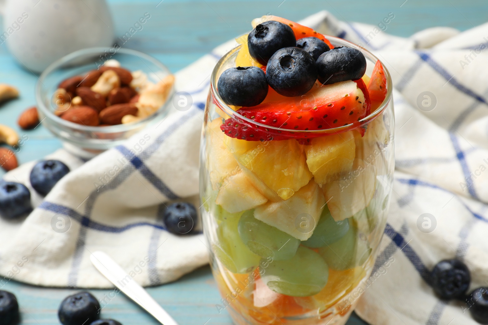 Photo of Delicious fruit salad, fresh berries and nuts on light blue wooden table, closeup