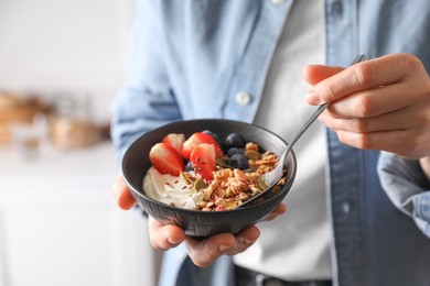 Photo of Woman eating tasty granola with berries, yogurt and seeds indoors, closeup