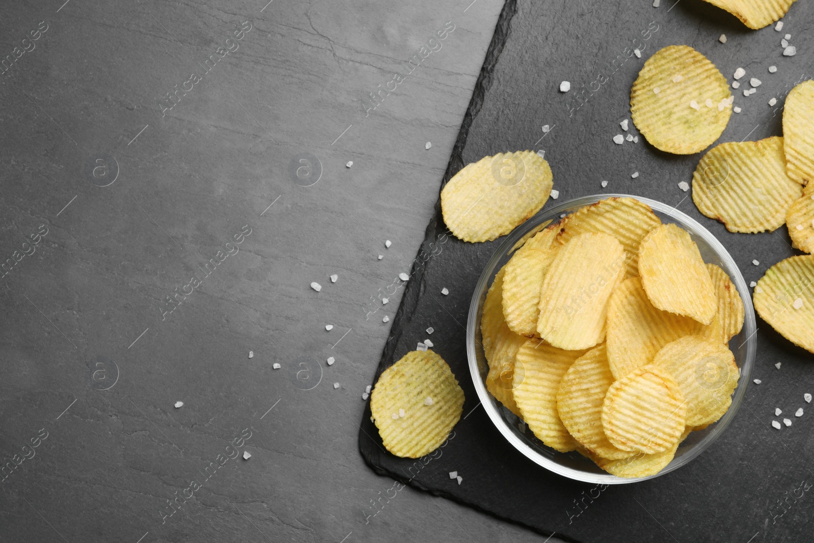 Photo of Slate board with potato chips on grey table, flat lay. Space for text