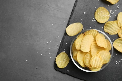 Photo of Slate board with potato chips on grey table, flat lay. Space for text