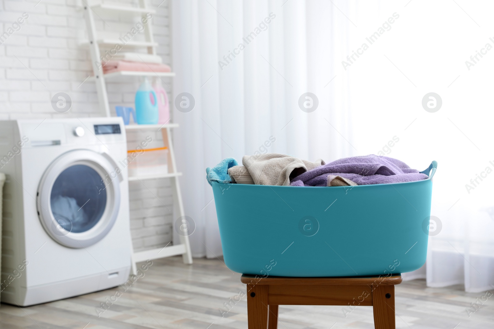 Photo of Plastic basket with dirty towels on table in laundry room, space for text
