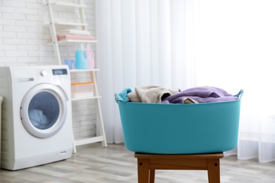 Plastic basket with dirty towels on table in laundry room, space for text