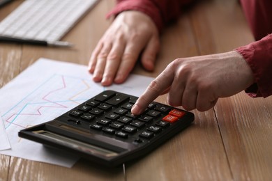 Photo of Man using calculator at wooden table, closeup