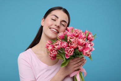 Happy young woman with beautiful bouquet on light blue background