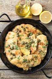 Delicious chicken piccata with herbs and lemon on wooden table, flat lay