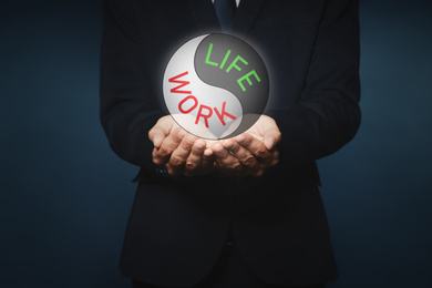 Businessman showing balance between life and work on dark background, closeup