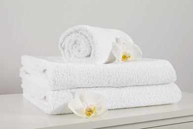Photo of Clean soft white towels with flowers on table against light grey background