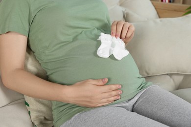 Photo of Pregnant woman sitting on sofa with baby socks indoors, closeup
